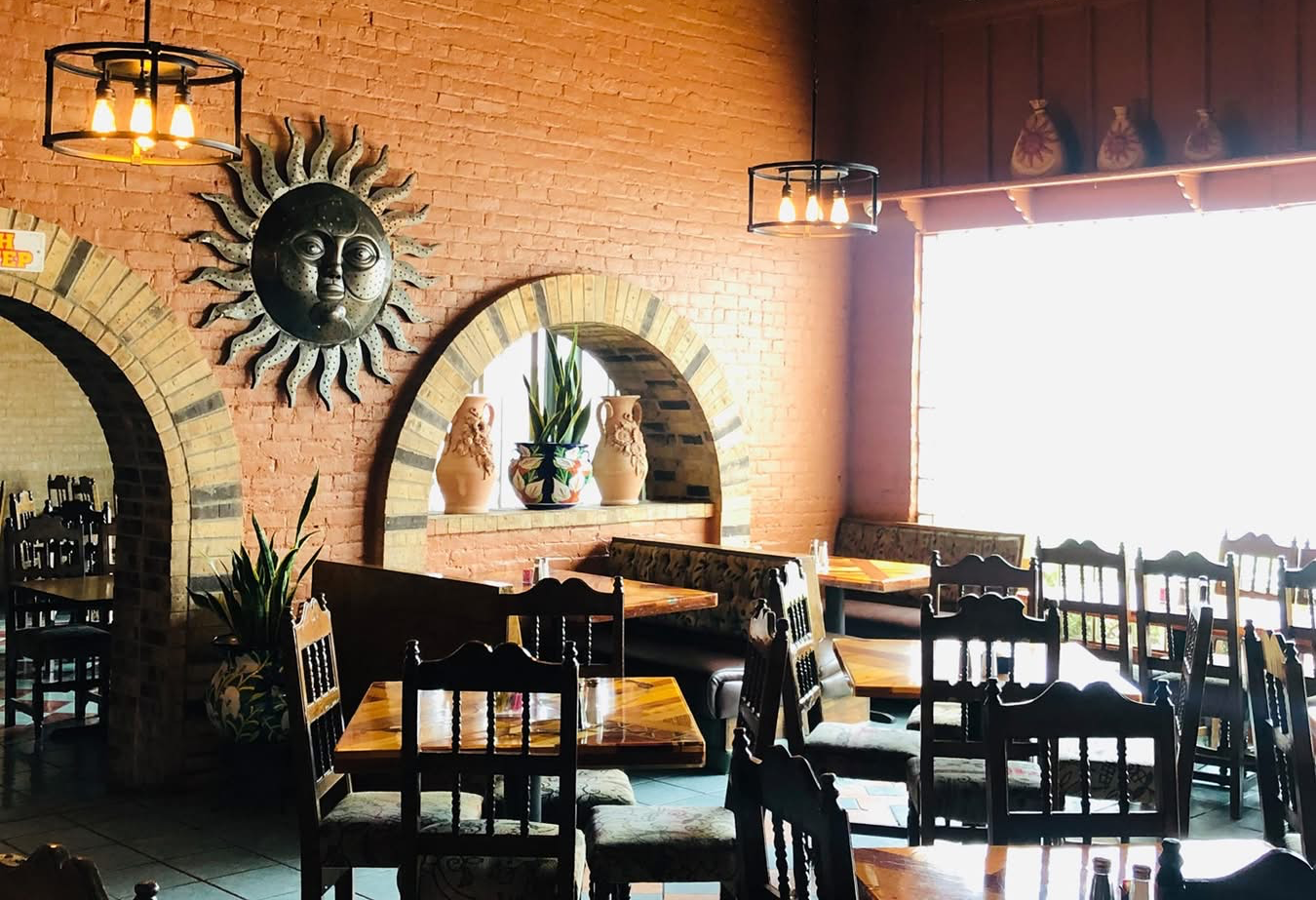 Warm, rustic dining room at Los Mariachis Tex-Mex with exposed brick walls, hand-carved wooden tables, and traditional Mexican décor