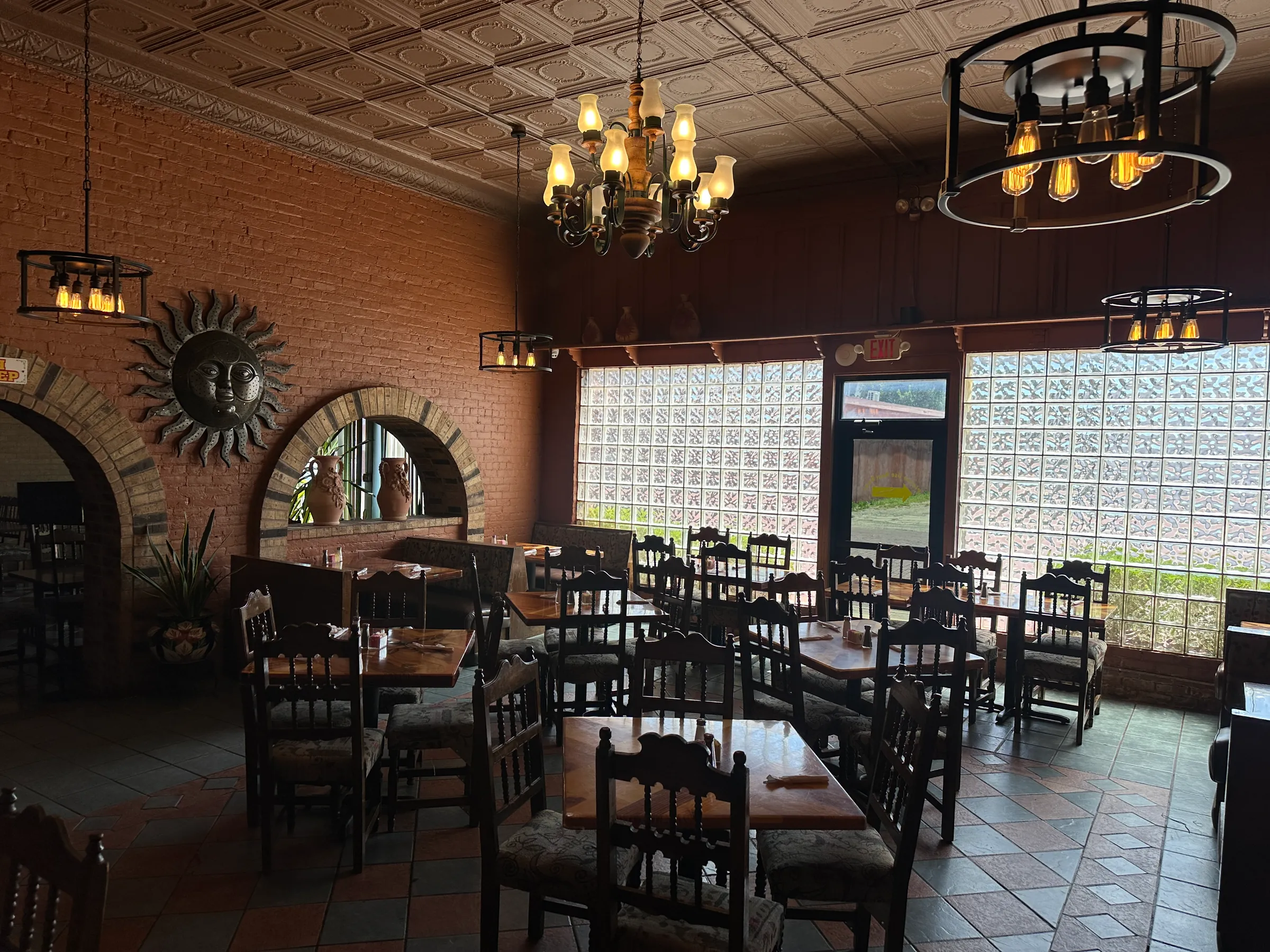 Warmly lit dining room at Los Mariachis Gainesville with glowing chandeliers, exposed brick arches, and rows of dark wooden tables.