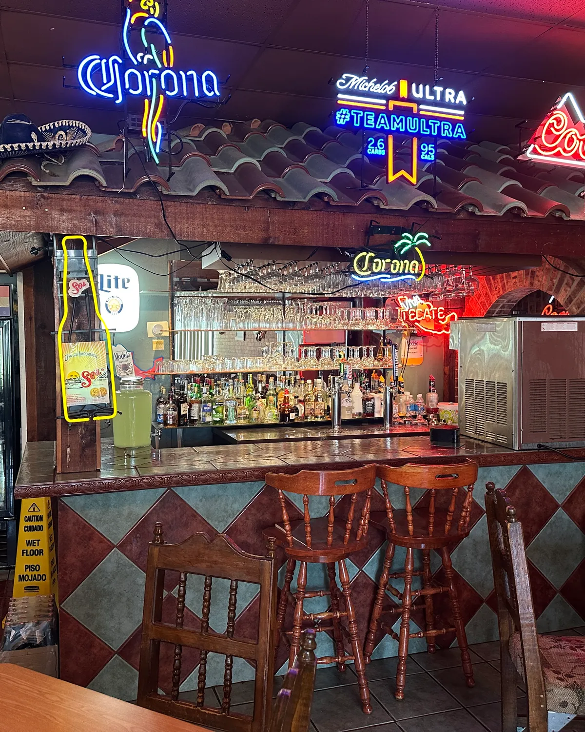 Rustic bar at Los Mariachis Tex-Mex featuring warm ambient lighting, exposed brick walls, hand-carved wooden bar stools, and traditional Mexican décor